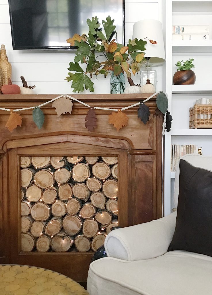 Wood fireplace decorated for fall with leather leaf garland strung on crocheted yarn and brass fasteners, with vase of fall leaves and sweater pumpkins on top of the mantele