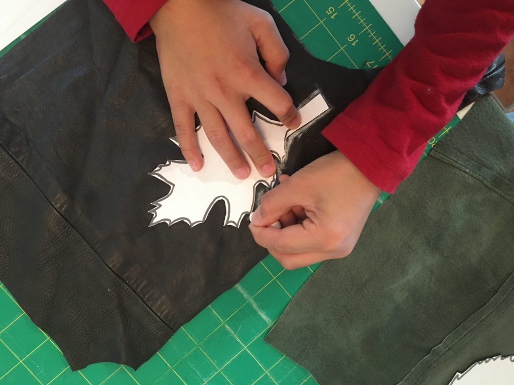 Childs hands tracing paper leaf template onto scrap of brown leather