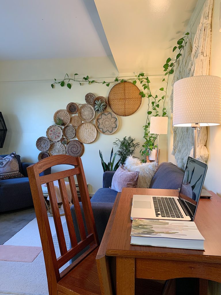 Living room with basket wall, houseplkants, color blocked rug and desk with Ikea lamps, urban outfitters planner