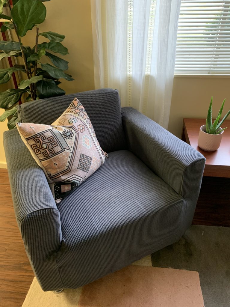 Grey slipcovered apartment chair with diy kilim pillow, blush color blocked rug and target boho curtain panel at window