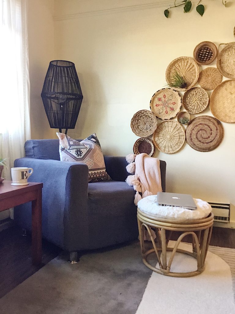 college apartment living room with diy basket wall, grey slip covered chair, kilim pillow and vintage stool with white fur cushion