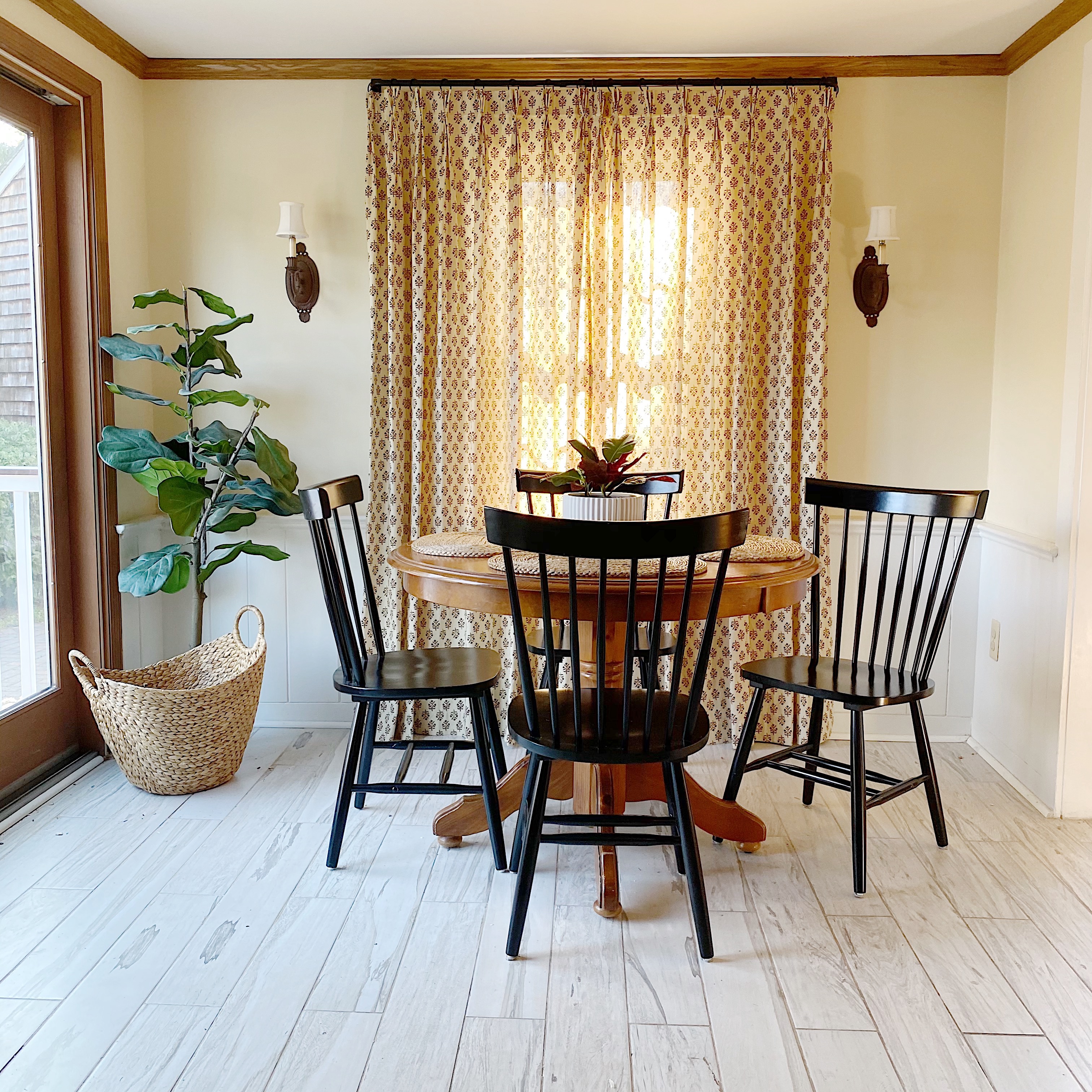 kitchen with ditsy print curtains over window, round kitchen table and black Windsor chairs on whitewashed tile floor