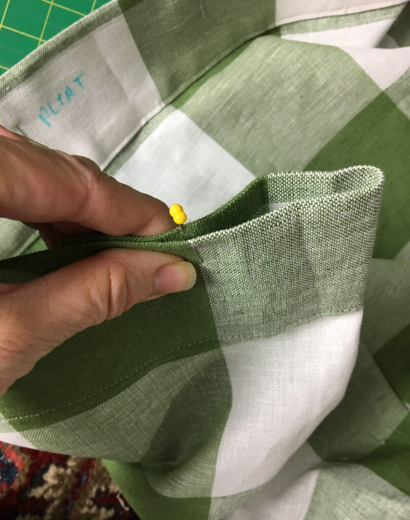 hand holding pinch pleat on green buffalo check curtain