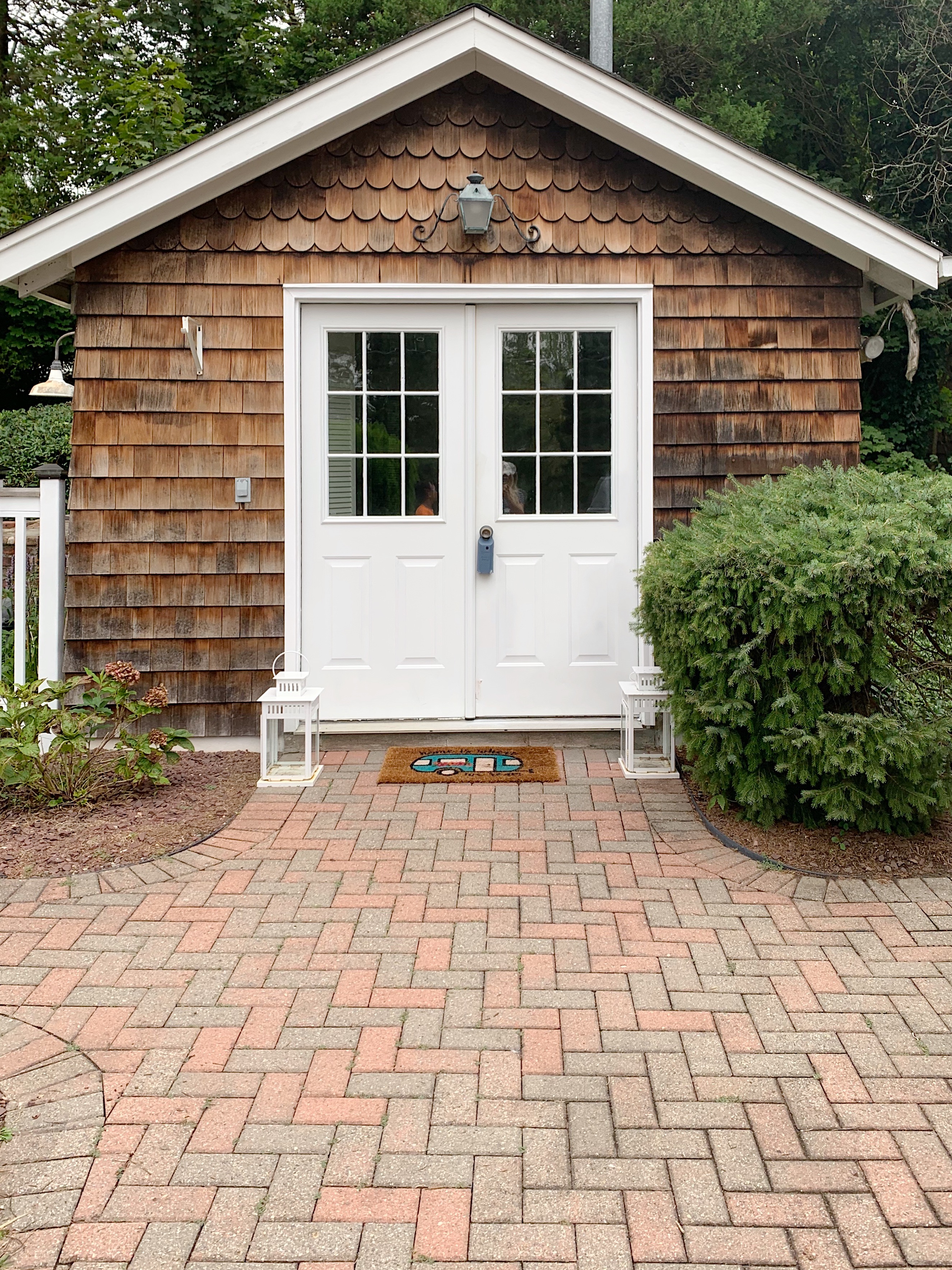 cedar clad cottage with white French doors and brick paver walkway