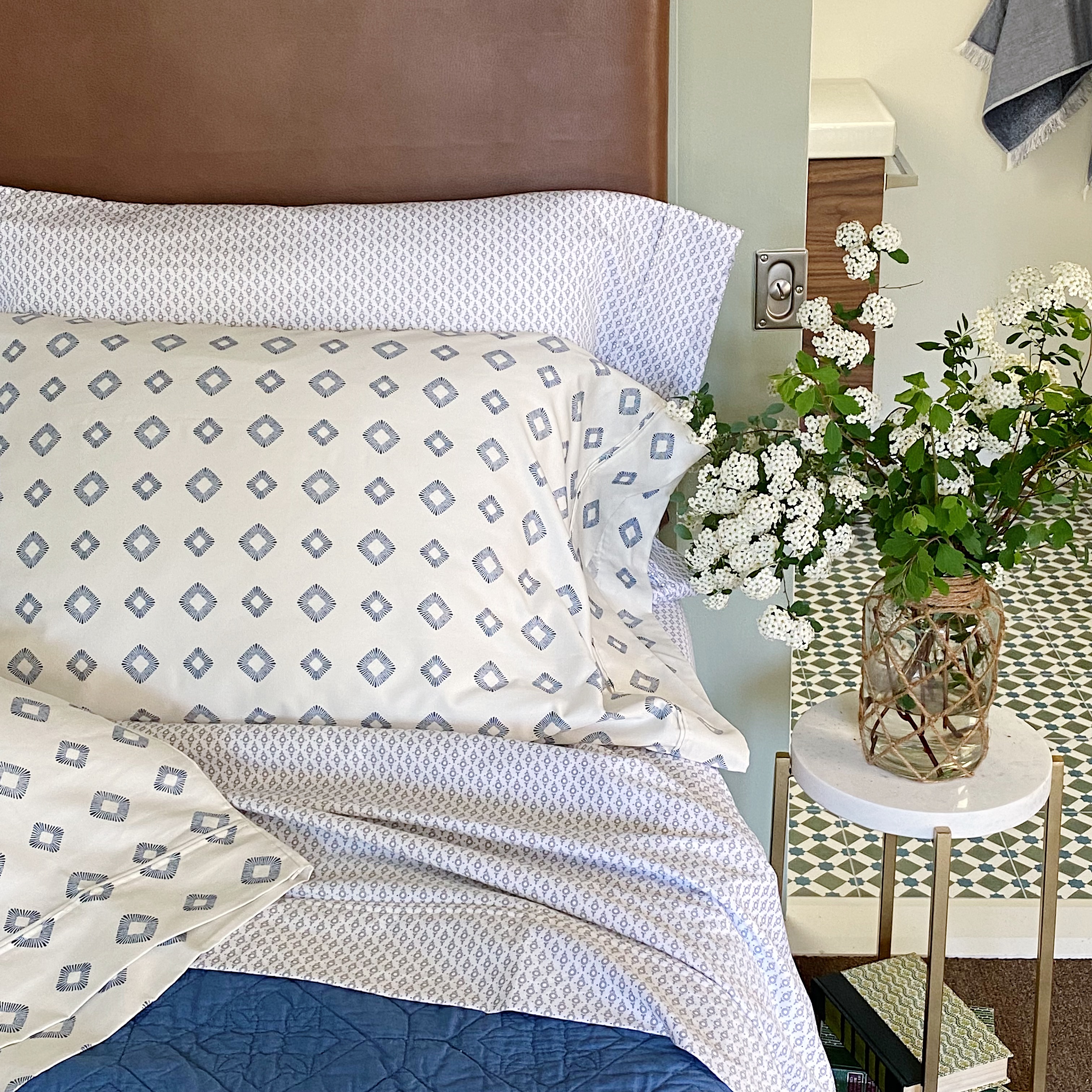 ditsy print sheets and pillows with leather headboard and flowers in vase