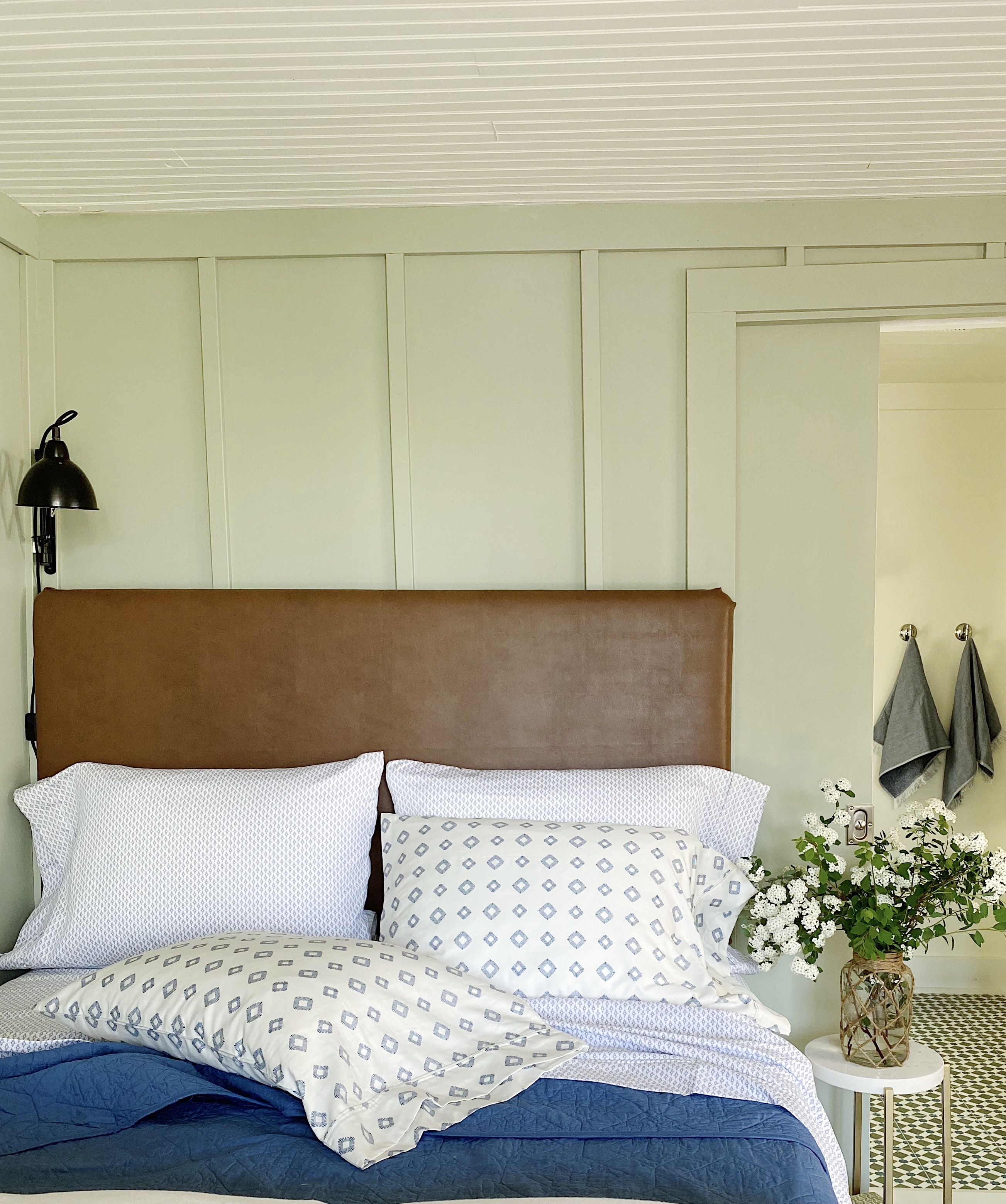 bed with leather headboard in front of green board and batten wall