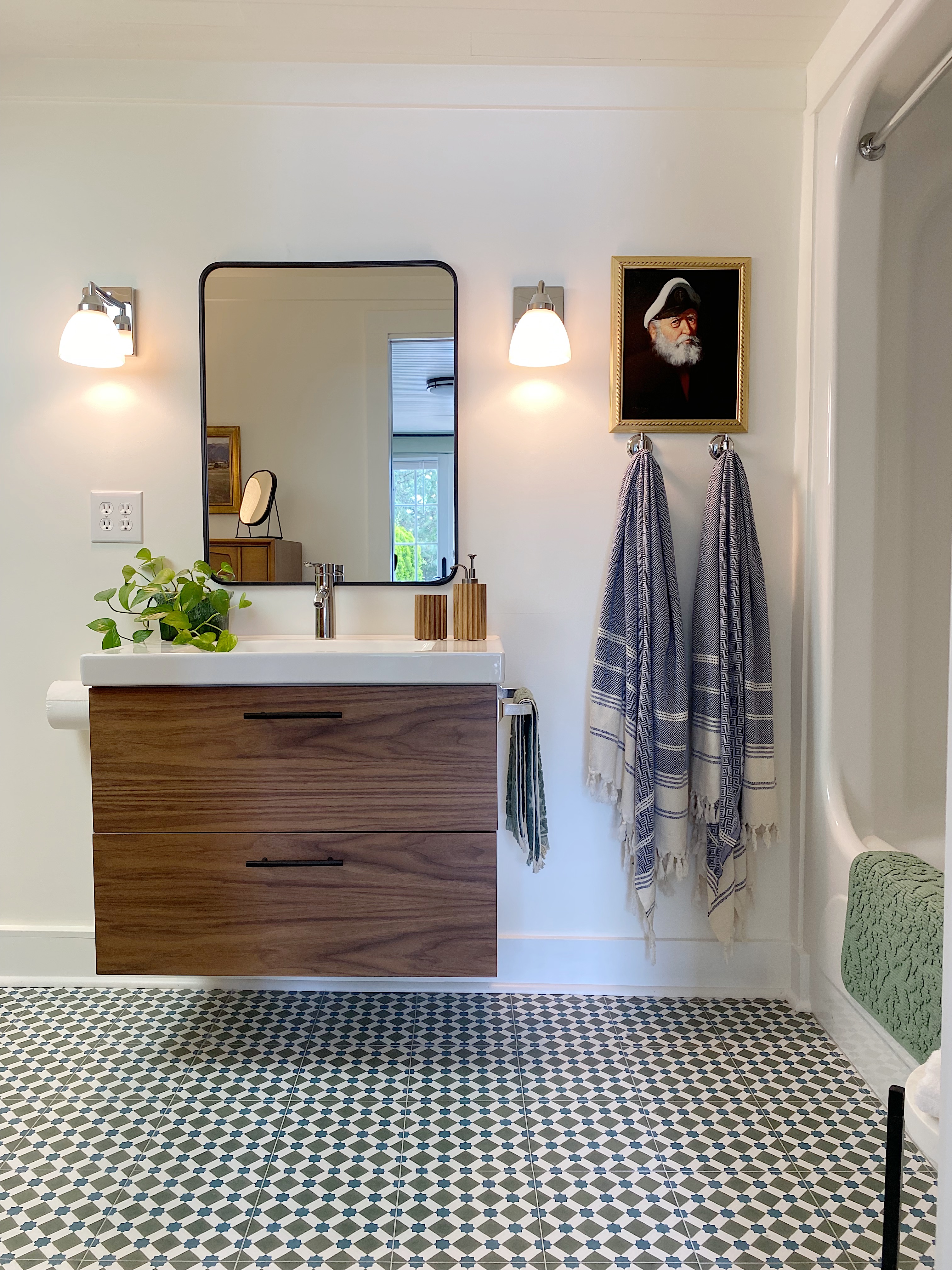 white bathroom with Ikea vanity with wood drawer fronts and black framed mirror and patterned floor tile