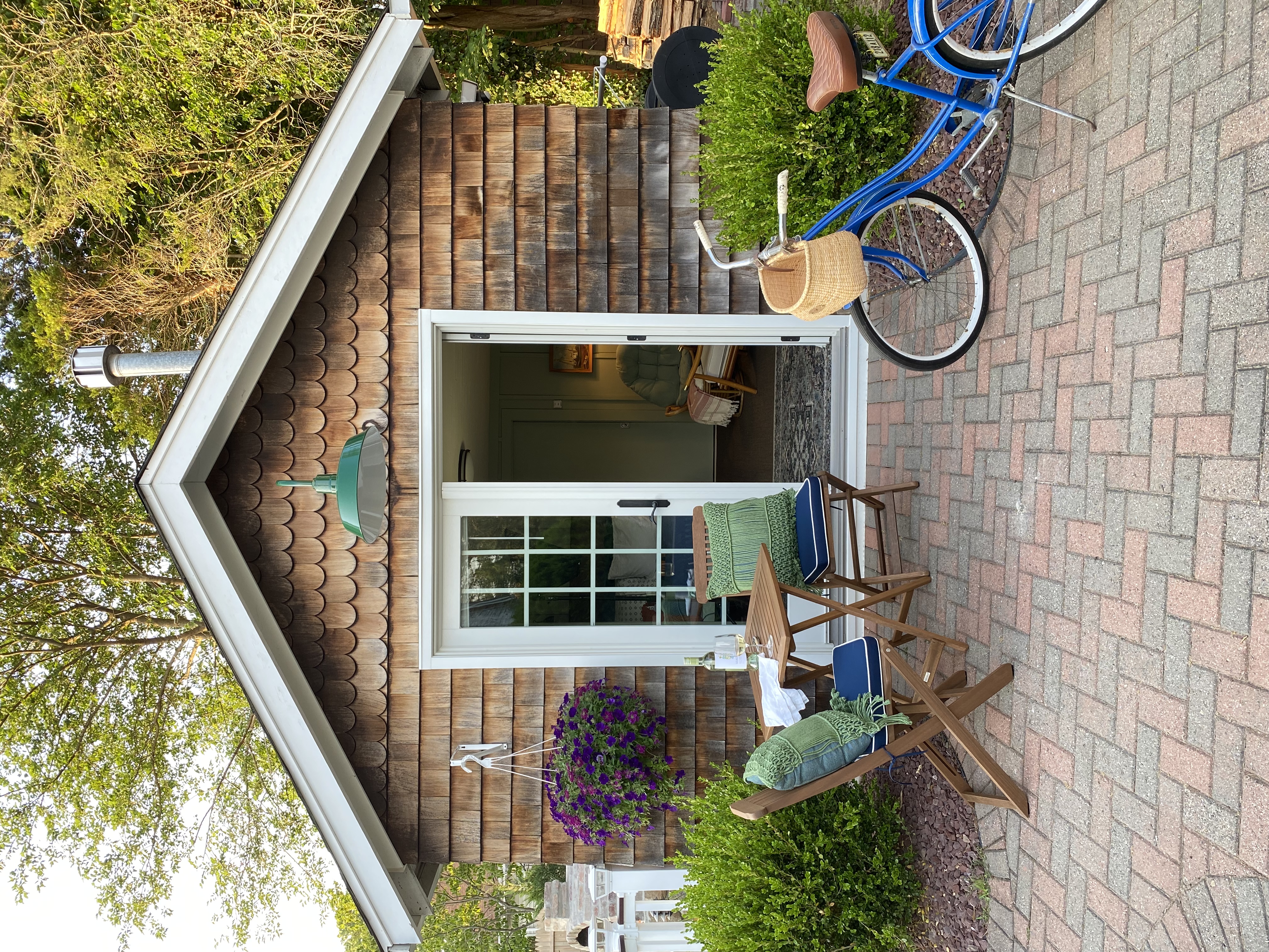 cedar shake cottage with white French doors, green overhead barn light, red brick walkway, teak bistro set and vintage blue cruiser bike