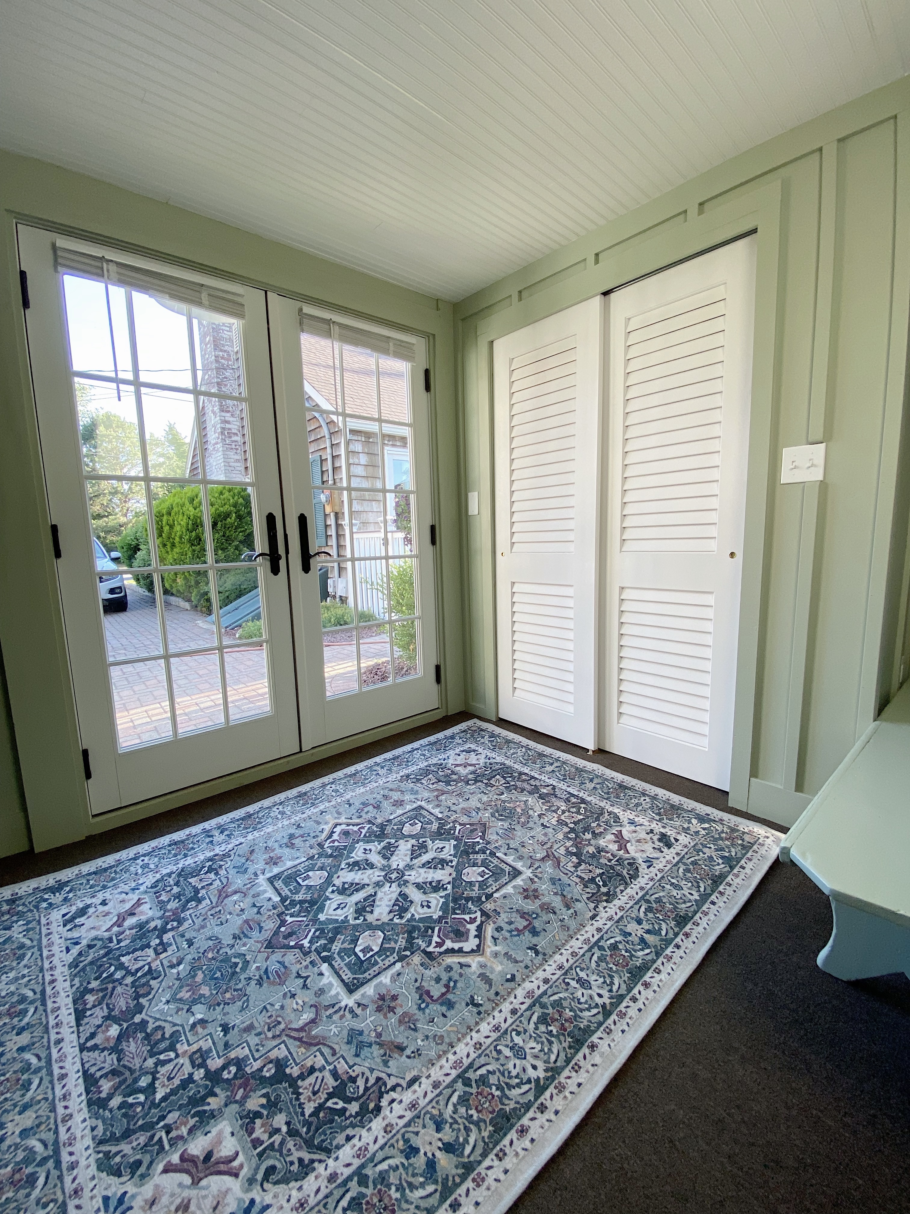 White louvered closet doors with green board and batten walls and oriental rug