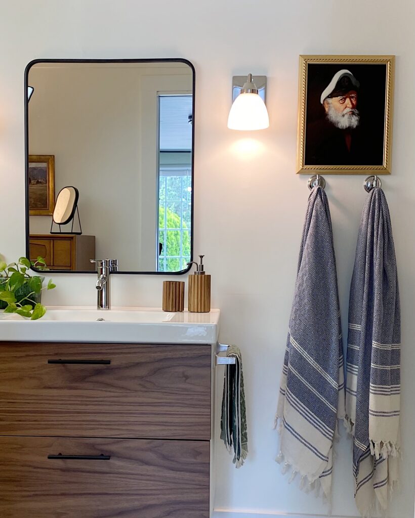 bathroom with sea captain print, blue Turkish towels, black framed mirror over Ikea vanity with wood fronts