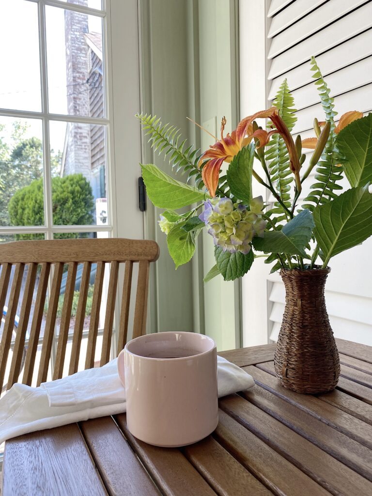 teak chair and table with wicker vase of day Lillies and blush cup with coffee