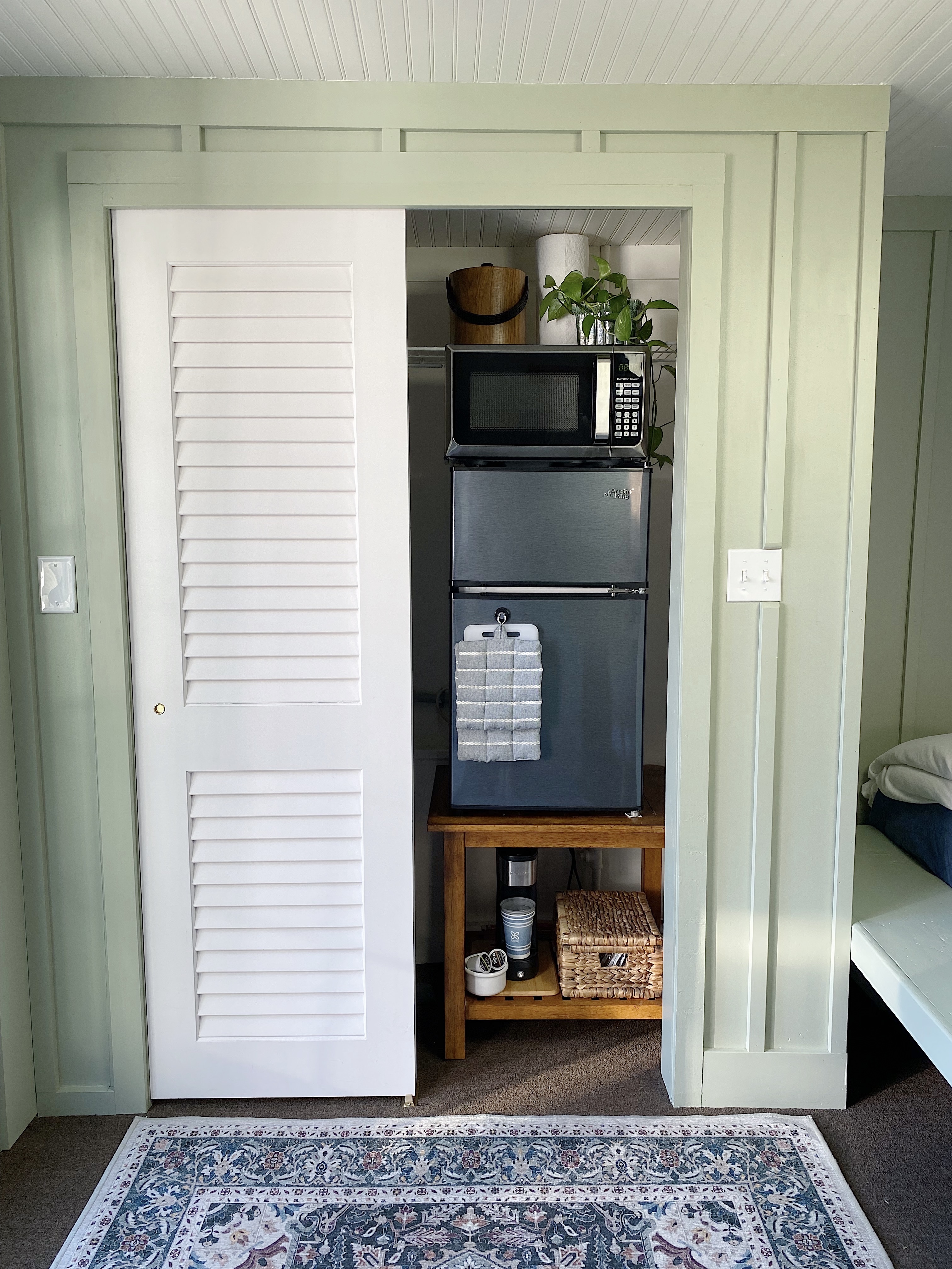 Mini kitchen in a closet with white louvered doors, green board and batten walls and oriental rug