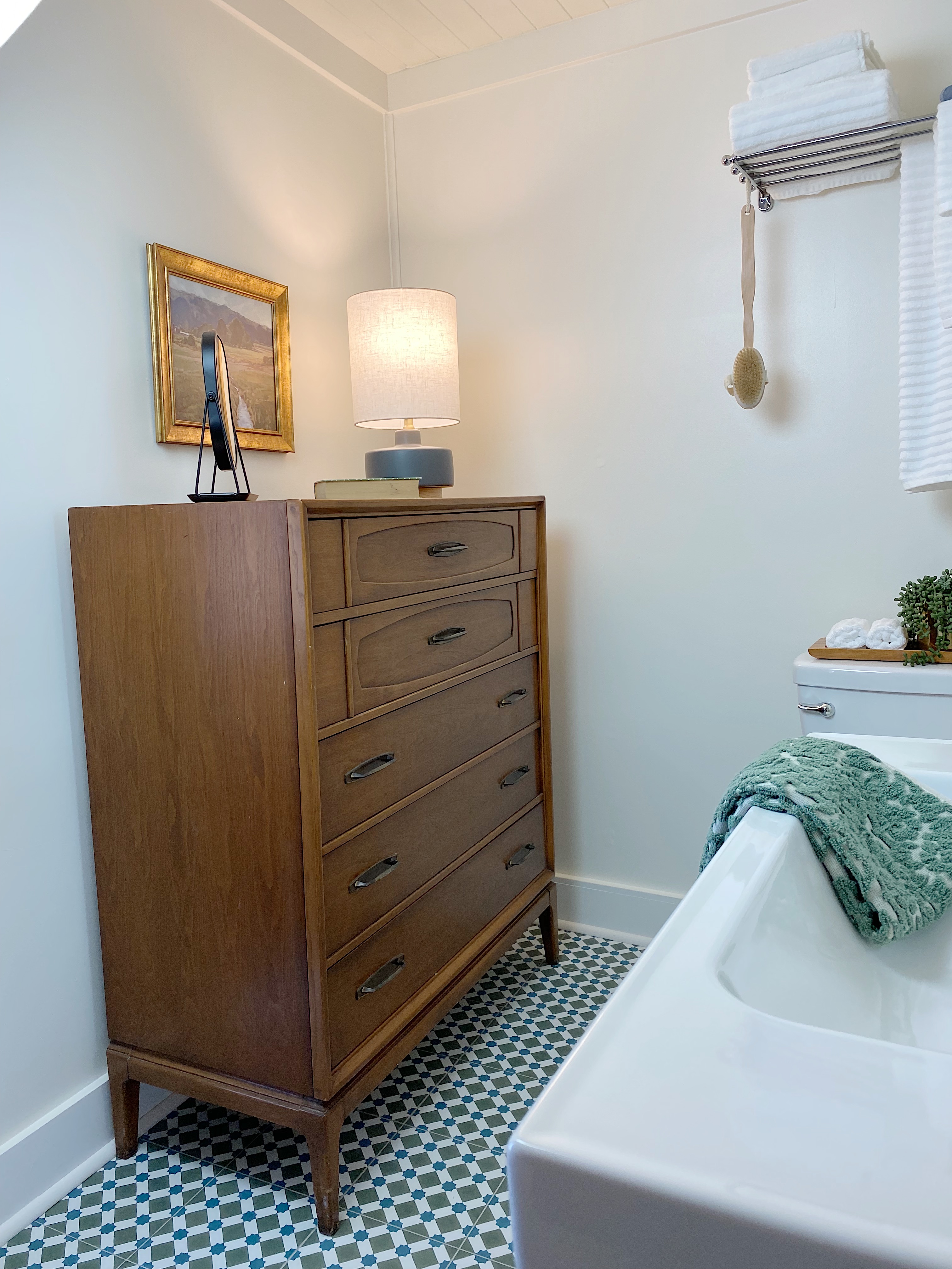 midcentury walnut dresser in bathroom with small lamp and framed art