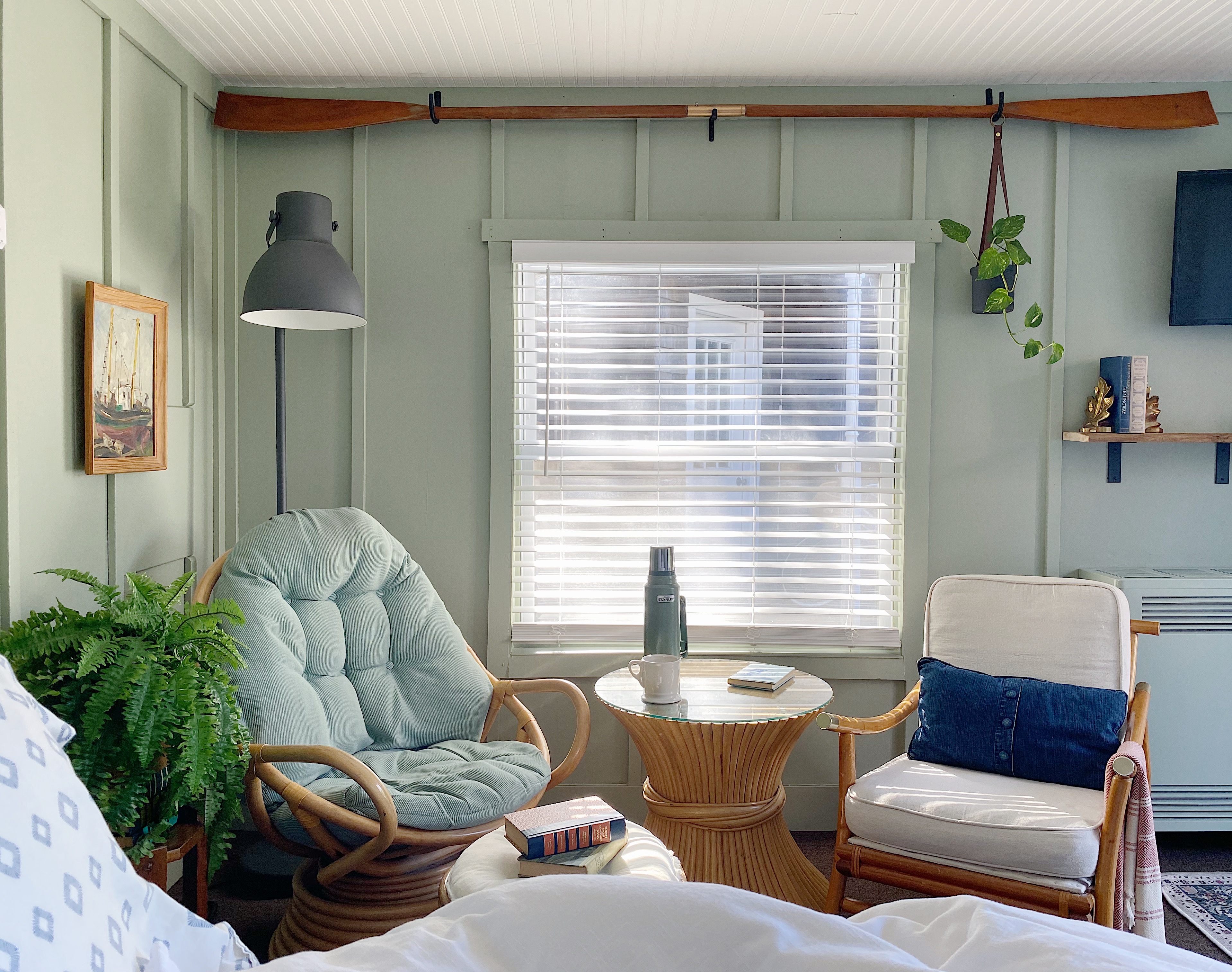 guest cottage sitting area with vintage rattan chairs, Ikea floor lamp, vintage wood oar above a window