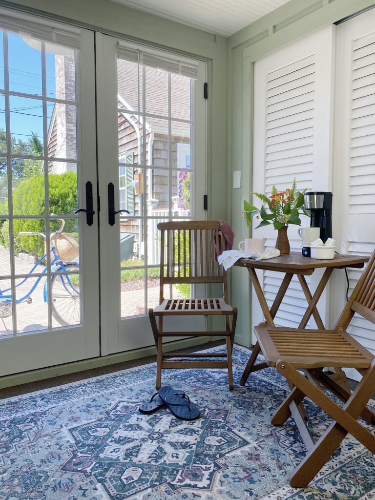 French doors with view to the outside, small wood bistro set with flowers and single cup coffee maker on top of machine washable huggable rug
