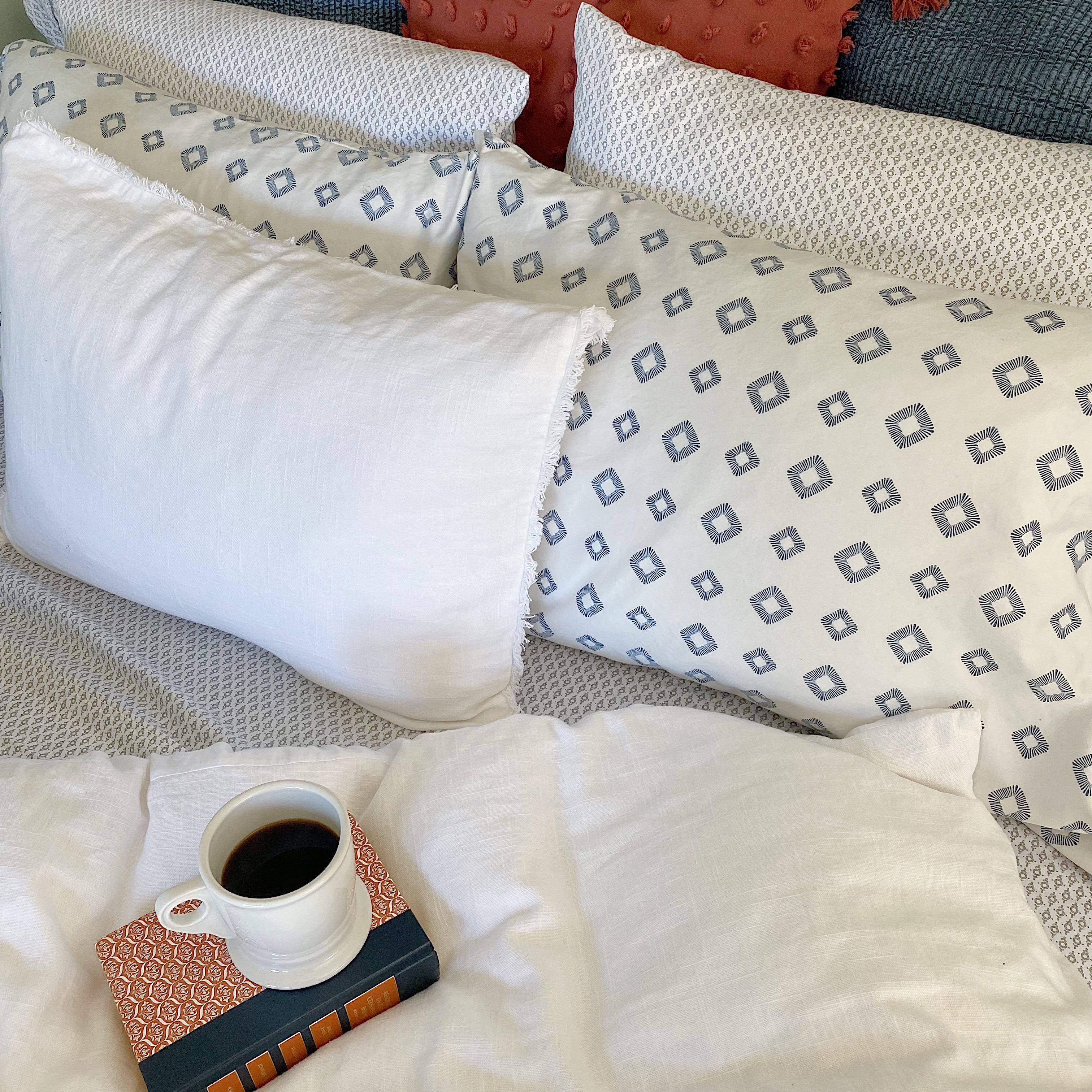 bed with white linen duvet and pillow, mix and match small print sheets, vintage book and cup of coffee