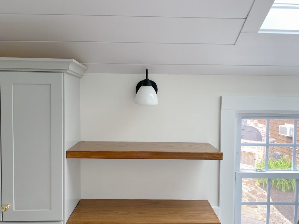 wood floating shelves with black wall sconce and shiplap ceiling