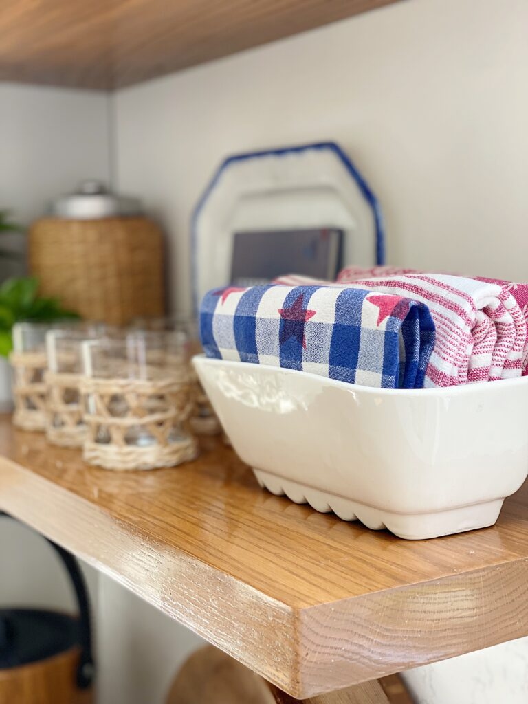 Rolled red, white and blue dish towels in vintage white rectangular bowl