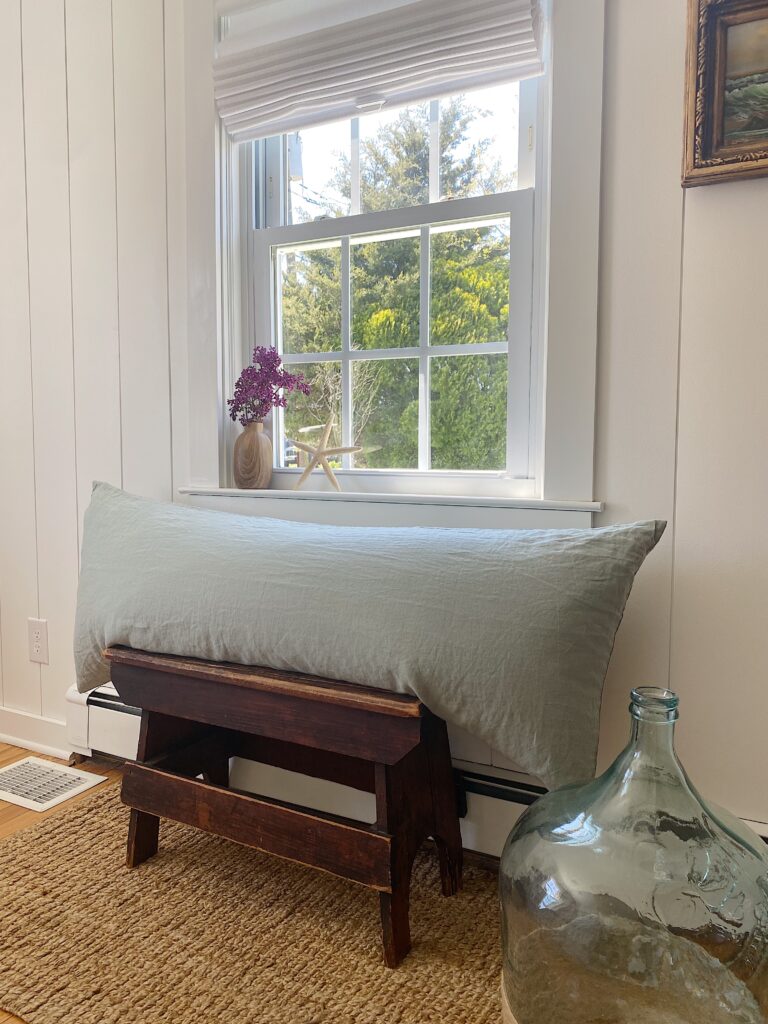 Sage green linen body pillow on vintage wooden bench in front of window and shiplap walls