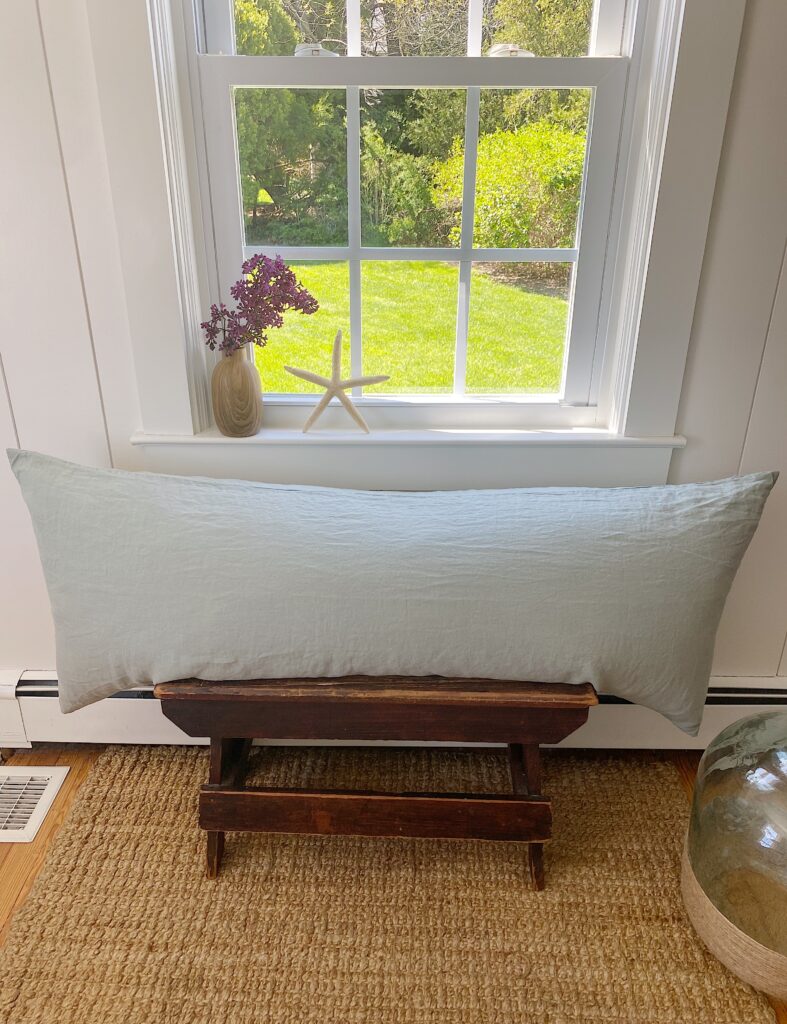 sage green linen body pillow on vintage wood bench against window and shiplap walls